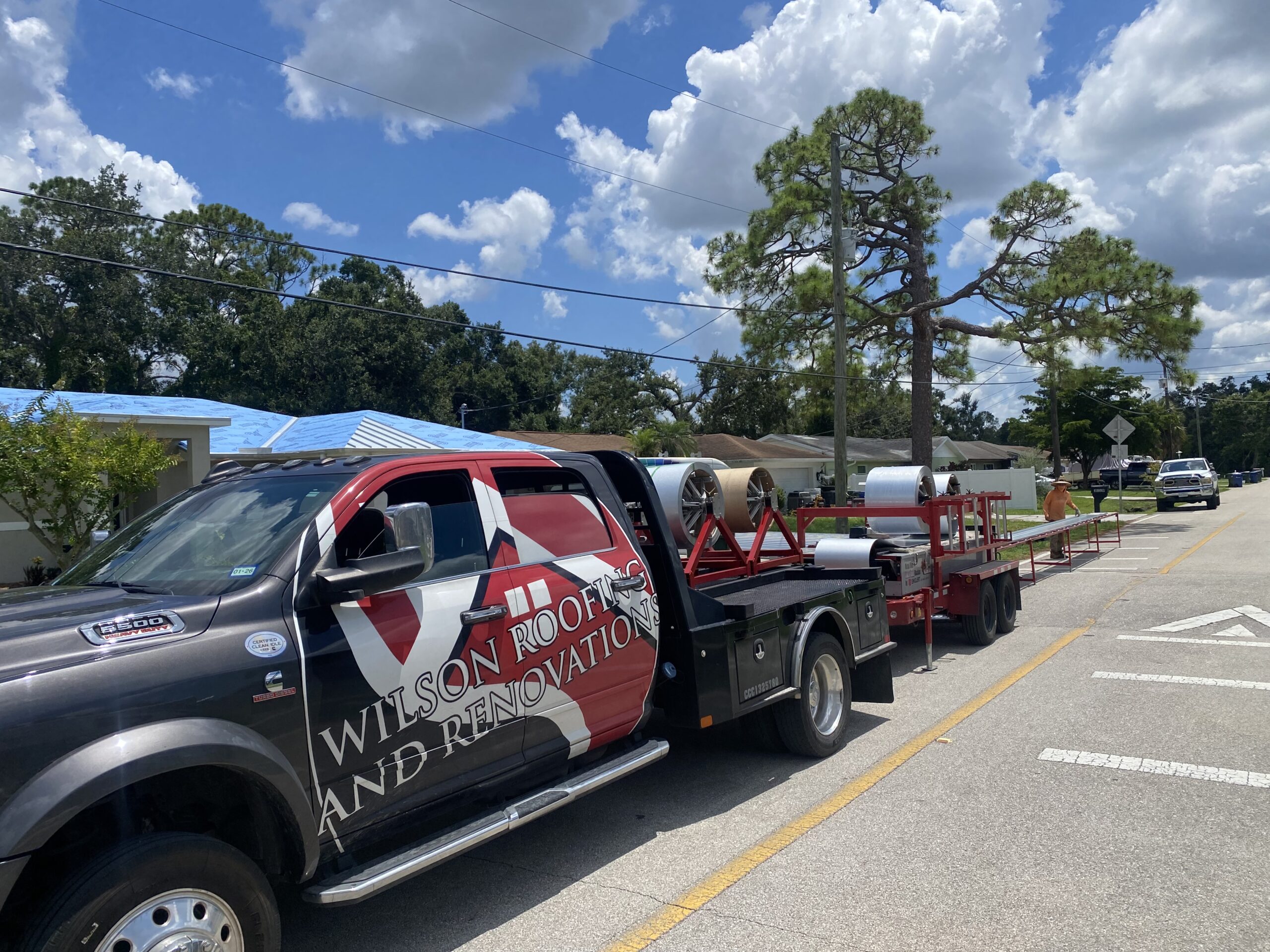 Wilson Roofing flatbed truck with metal coils and a rollforming machine parked at a residential re-roof